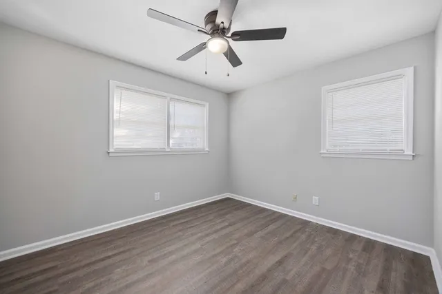 an empty room with wooden floor ceiling fan and windows