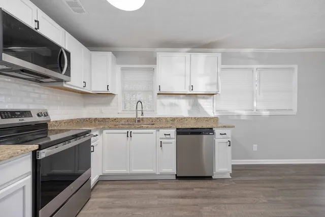 a kitchen with stainless steel appliances granite countertop a stove top oven a sink dishwasher and white cabinets with wooden floor