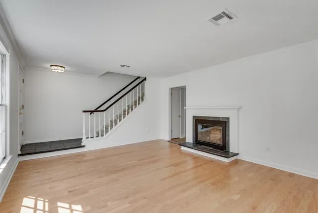a view of an empty room with wooden floor fireplace and a window