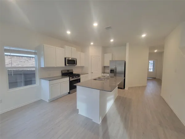 a kitchen with kitchen island stainless steel appliances a sink stove refrigerator and cabinets