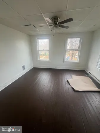 an empty room with wooden floor windows and fan