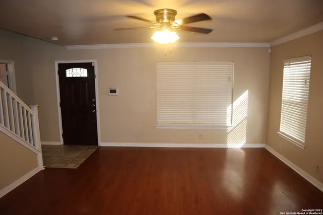 an empty room with wooden floor fan and windows