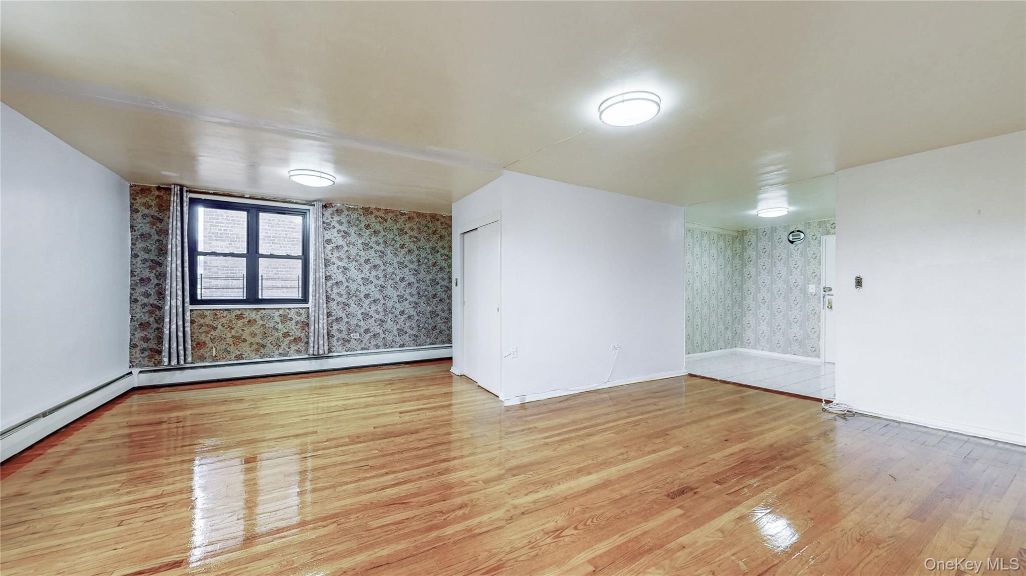 99-35 59th Avenue, Unit 4E Queens, NY 11368 - Photo 6 of 22 Empty room with wallpapered walls, light wood-style floors, and a baseboard radiator