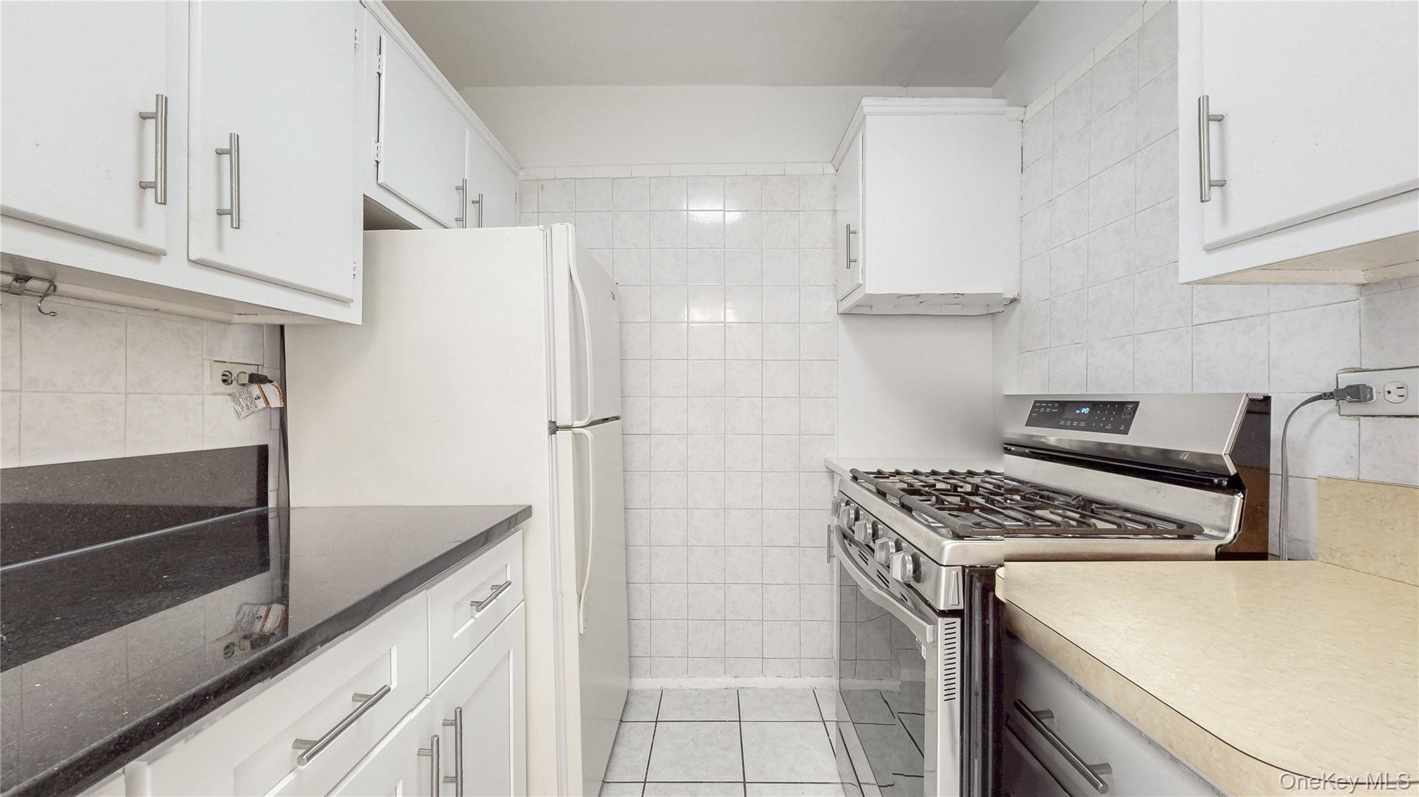 99-35 59th Avenue, Unit 4E Queens, NY 11368 - Photo 9 of 22 Kitchen with gas range, white cabinetry, tile walls, light tile patterned flooring, and freestanding refrigerator