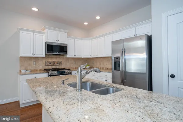 a kitchen with stainless steel appliances granite countertop a refrigerator a stove a sink a microwave and white cabinets