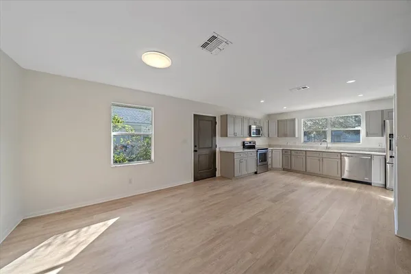 a large white kitchen with stainless steel appliances granite countertop a stove top oven a sink dishwasher and white cabinets with wooden floor