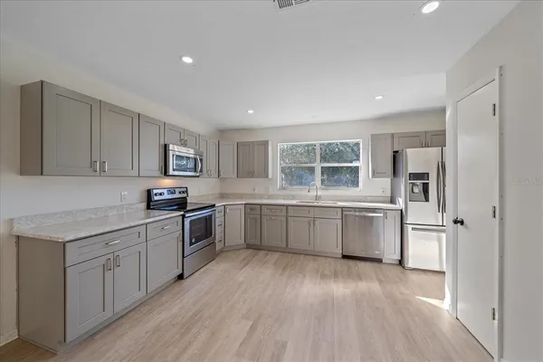 a kitchen with stainless steel appliances granite countertop a stove a sink dishwasher a refrigerator and white cabinets with wooden floor