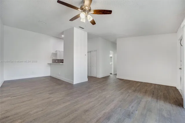 an empty room with wooden floor ceiling fan and windows