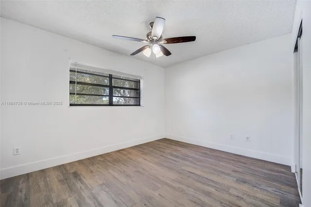 an empty room with wooden floor ceiling fan and windows