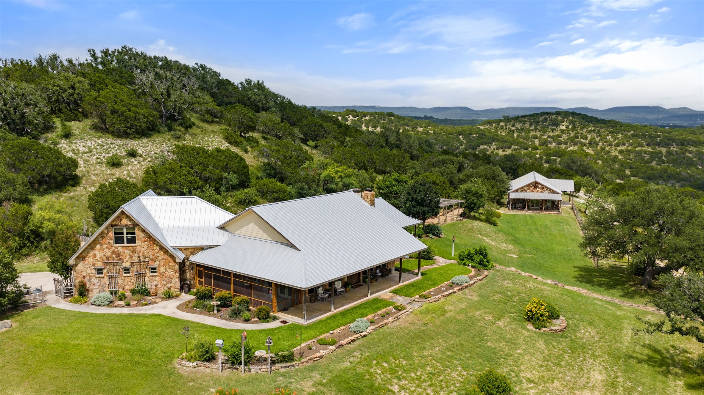 8400 Ranch Road 1431 Marble Falls, TX 78654 - Photo 1 of 30 Perched on a verdant hillside, this stone and metal-roofed estate offers serene views of the surrounding hills.