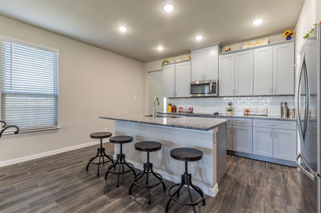 626 Ruthye Lane Pilot Point, TX 76258 - Photo 16 of 27 Kitchen featuring dark stone counters, custom gray cabinetry, a breakfast bar, appliances with stainless steel finishes, and recessed lighting