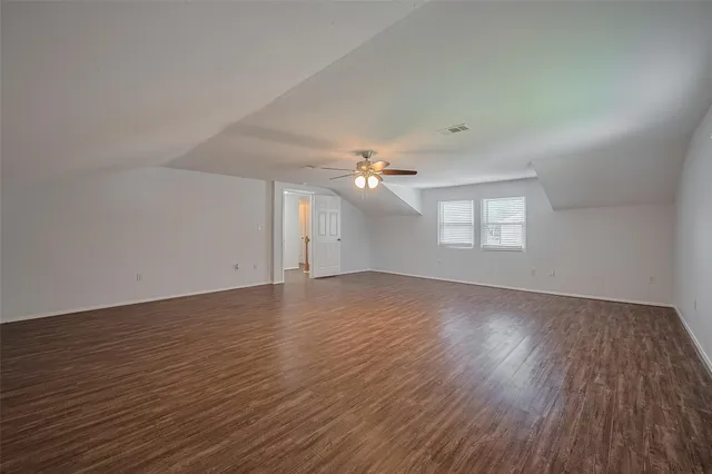 an empty room with wooden floor ceiling fan and windows