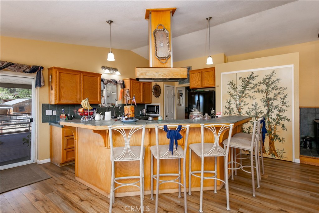 10960 Steinhoff Road Frazier Park, CA 93225 - Photo 25 of 46 An expansive, open-concept view highlighting the home's main entertaining hub. The spacious kitchen features a large wrap-around breakfast bar island with comfortable counter seating, extensive warm oak cabinetry, and unique overhead lighting, flowing seamlessly into a bright dining area perfect for gatherings.
