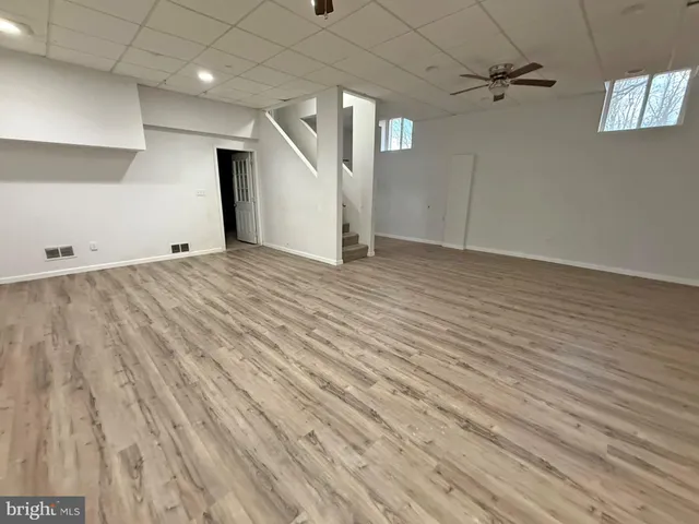 an empty room with wooden floor ceiling fan and windows