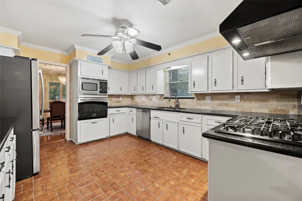 a kitchen with granite countertop a refrigerator a stove a sink dishwasher and white cabinets with wooden floor