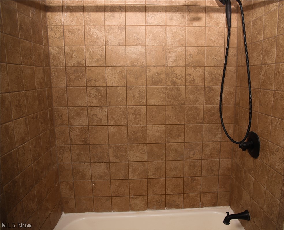 1087 Krumroy Road Akron, OH 44306 - Photo 21 of 23 Shower enclosure featuring tan square tiles, white tub base, matte black shower head with hose, and matte black tub spout