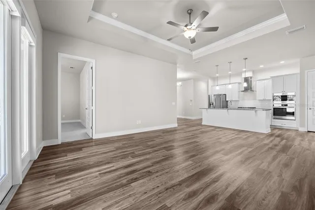 a view of an empty room and kitchen view with wooden floor