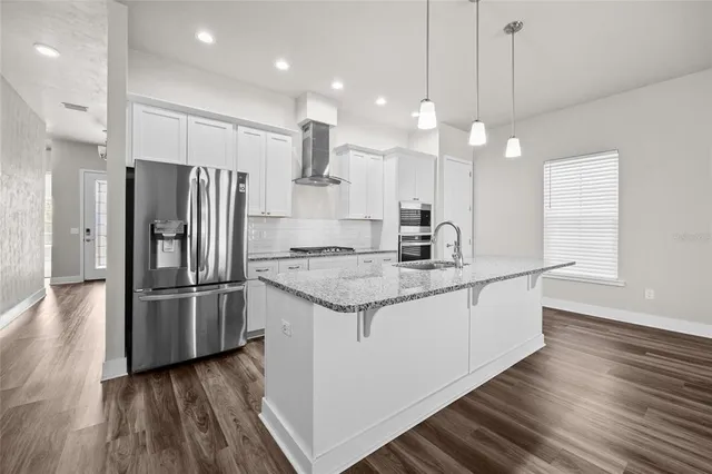 a kitchen with stainless steel appliances granite countertop a refrigerator a sink a stove and a wooden floors