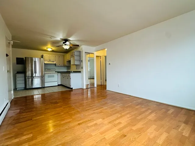 a view of empty room with wooden floor and a kitchen