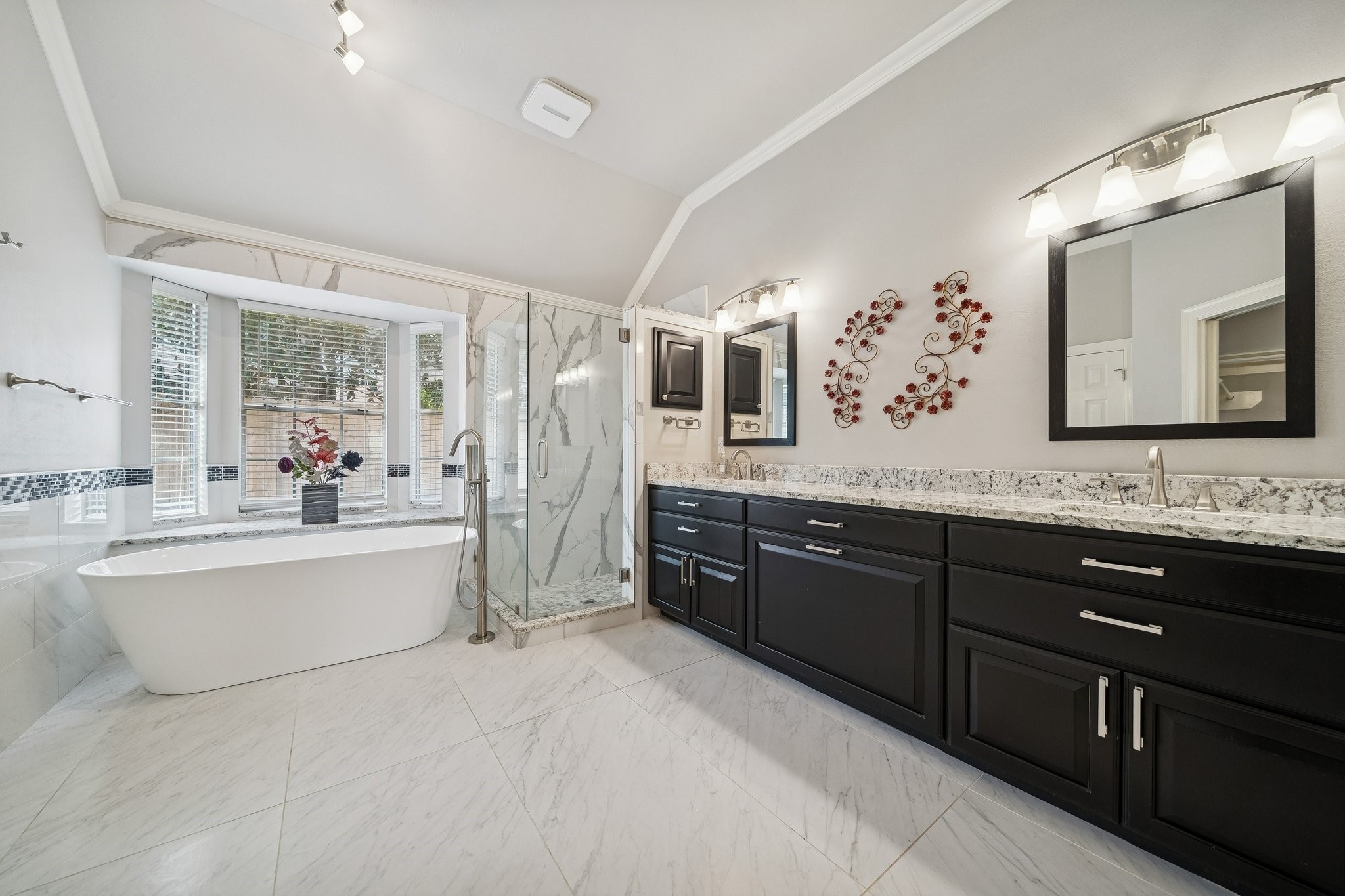 2114 Lytham Lane Katy, TX 77450 - Photo 13 of 29 This spacious primary bathroom features a modern freestanding tub beneath large windows, a sleek glass-enclosed shower, and a double vanity with elegant dark cabinets and granite countertops. Bright lighting and decorative accents enhance the luxurious feel.