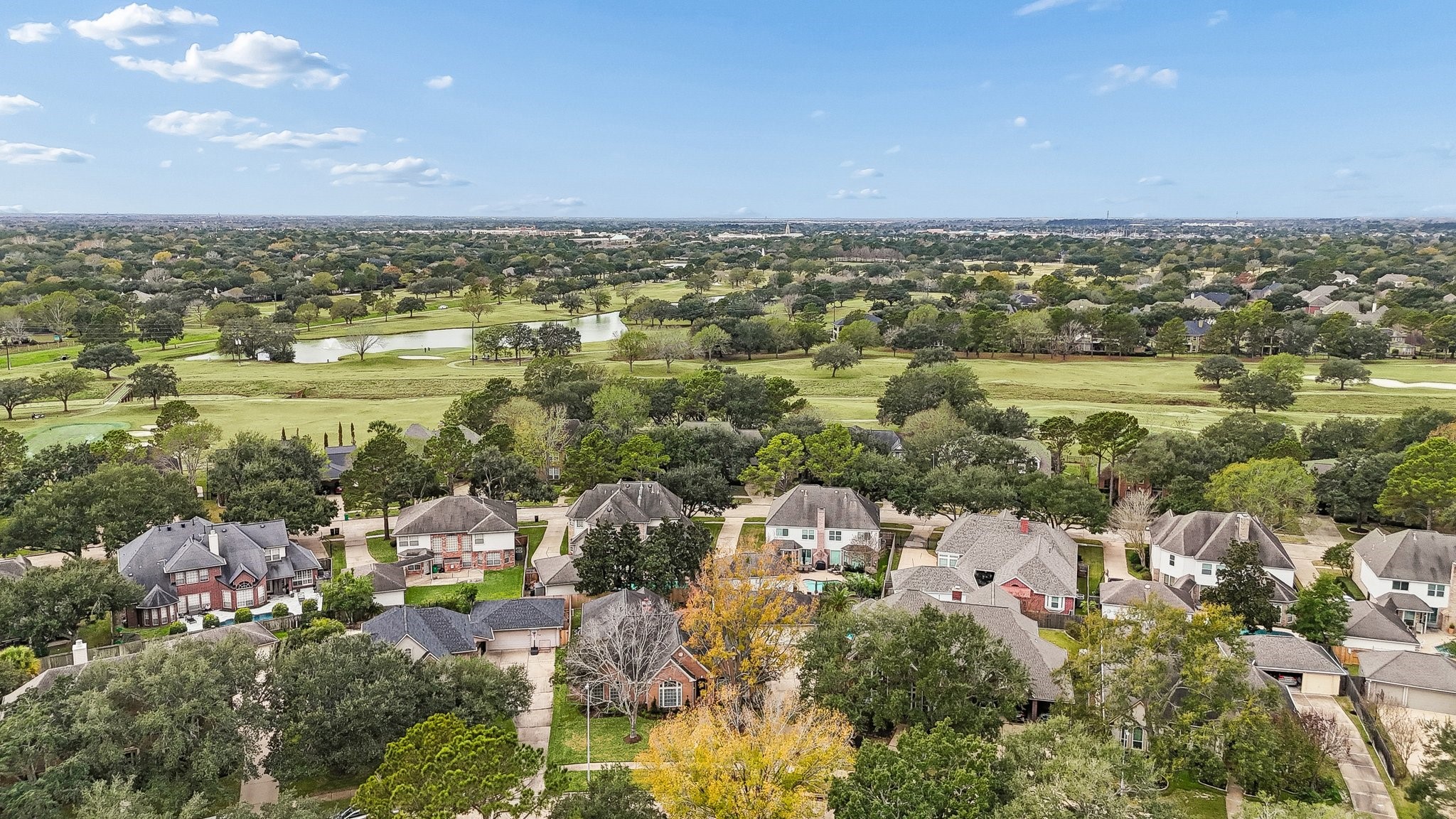 2114 Lytham Lane Katy, TX 77450 - Photo 25 of 29 This photo showcases a suburban neighborhood with spacious homes surrounded by lush greenery. In the background, there is a golf course with a small pond, offering scenic views and a serene atmosphere. The area appears to be well-maintained and ideal for families seeking a peaceful environment.