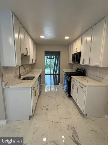 a large white kitchen with a sink and dishwasher a stove top oven with wooden floor