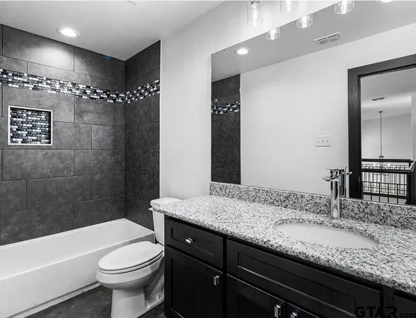 a bathroom with a granite countertop sink a toilet a mirror a bathtub and shower