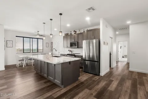 a kitchen with stainless steel appliances granite countertop a refrigerator a sink dishwasher a stove and a dining table with wooden floor