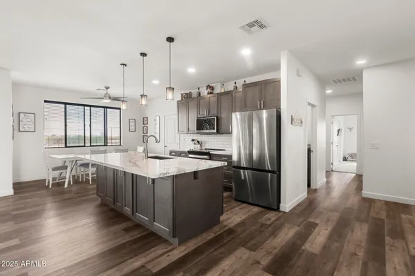 a kitchen with stainless steel appliances granite countertop a refrigerator a sink dishwasher a stove and a dining table with wooden floor