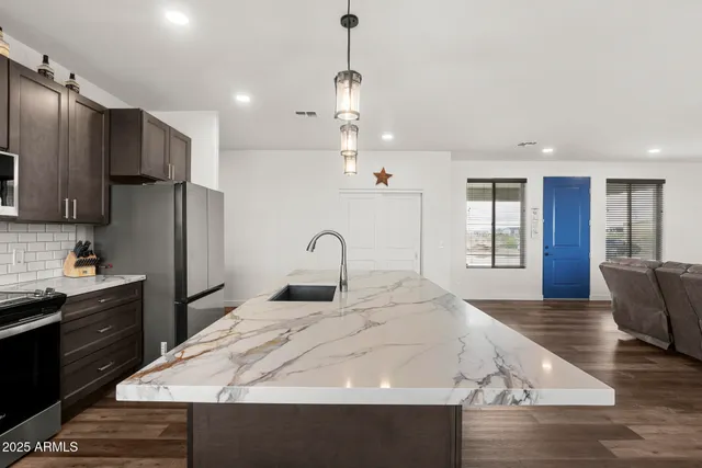 a kitchen with stainless steel appliances kitchen island granite countertop a refrigerator a stove and a sink with wooden floor