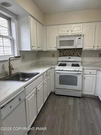 a white kitchen with granite countertop a stove top oven a sink and dishwasher