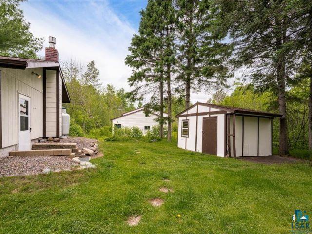 3616 Lavaque Road Hermantown, MN 55811 - Photo 20 of 43 Spacious backyard featuring a white storage shed with brown trim, a gravel patio, and mature evergreen trees
