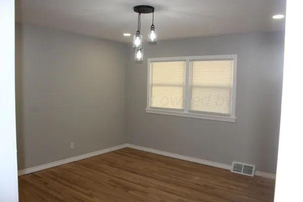 an empty room with wooden floor chandelier and windows