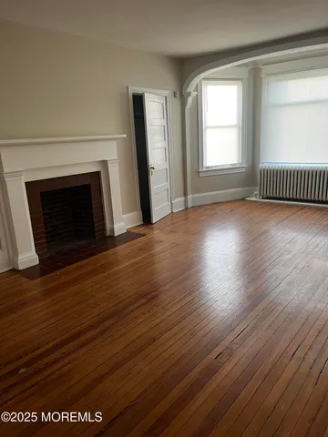 an empty room with wooden floor fireplace and windows