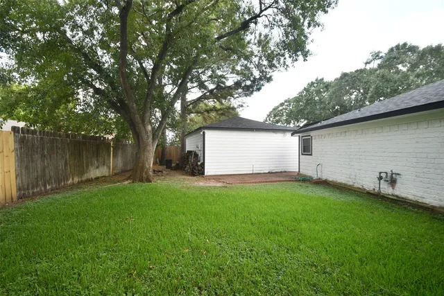 a view of a backyard with large trees and wooden fence
