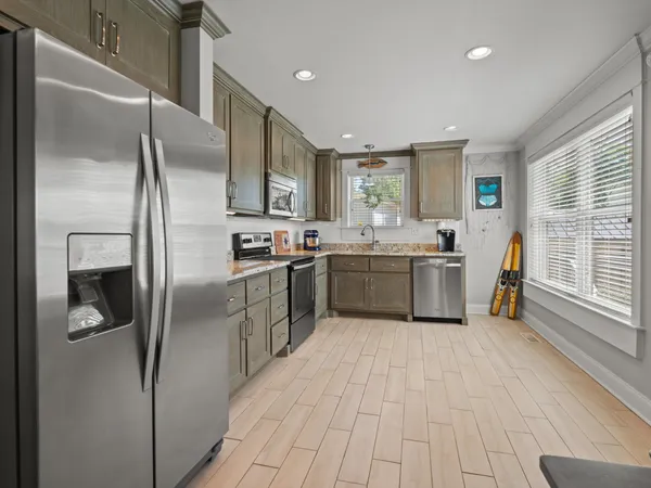 a kitchen with stainless steel appliances granite countertop a refrigerator a sink a stove and white cabinets with wooden floor