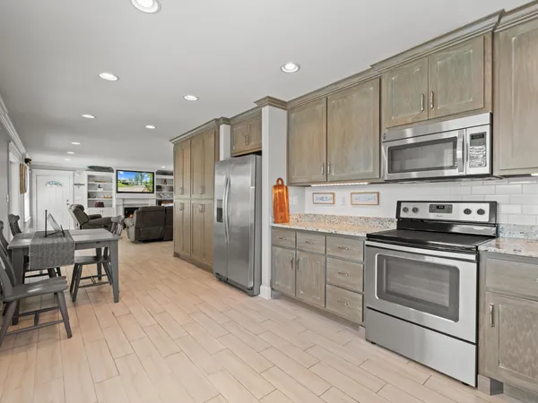 a kitchen with stainless steel appliances granite countertop a stove a refrigerator a microwave oven with white cabinets and wooden floor