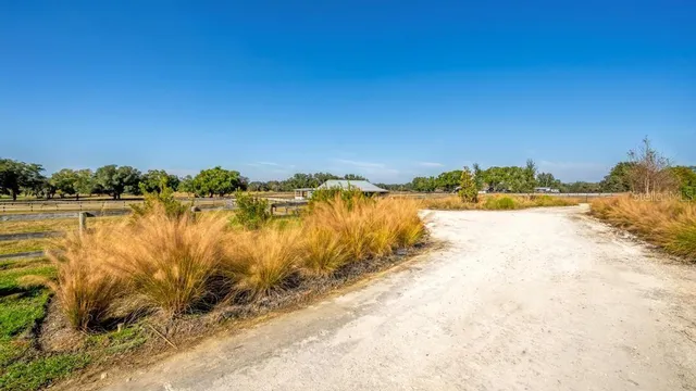a blue swimming pool is in a big yard with lawn chairs under an umbrella