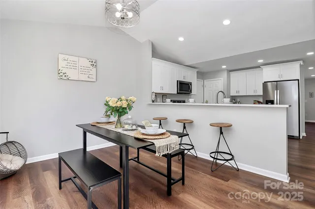 a kitchen with stainless steel appliances granite countertop a refrigerator a stove a sink a dining table and chairs with wooden floor