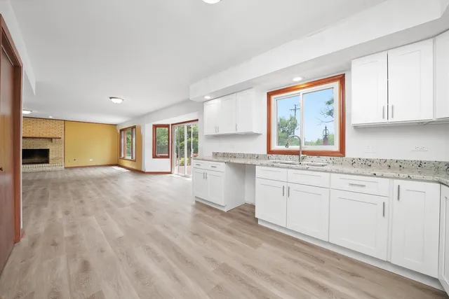 a kitchen with granite countertop a stove a sink and white cabinets with wooden floor next to windows