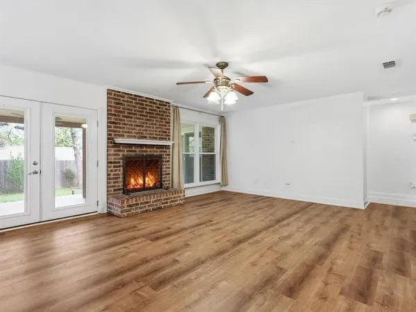 a view of an empty room with wooden floor fireplace and a window