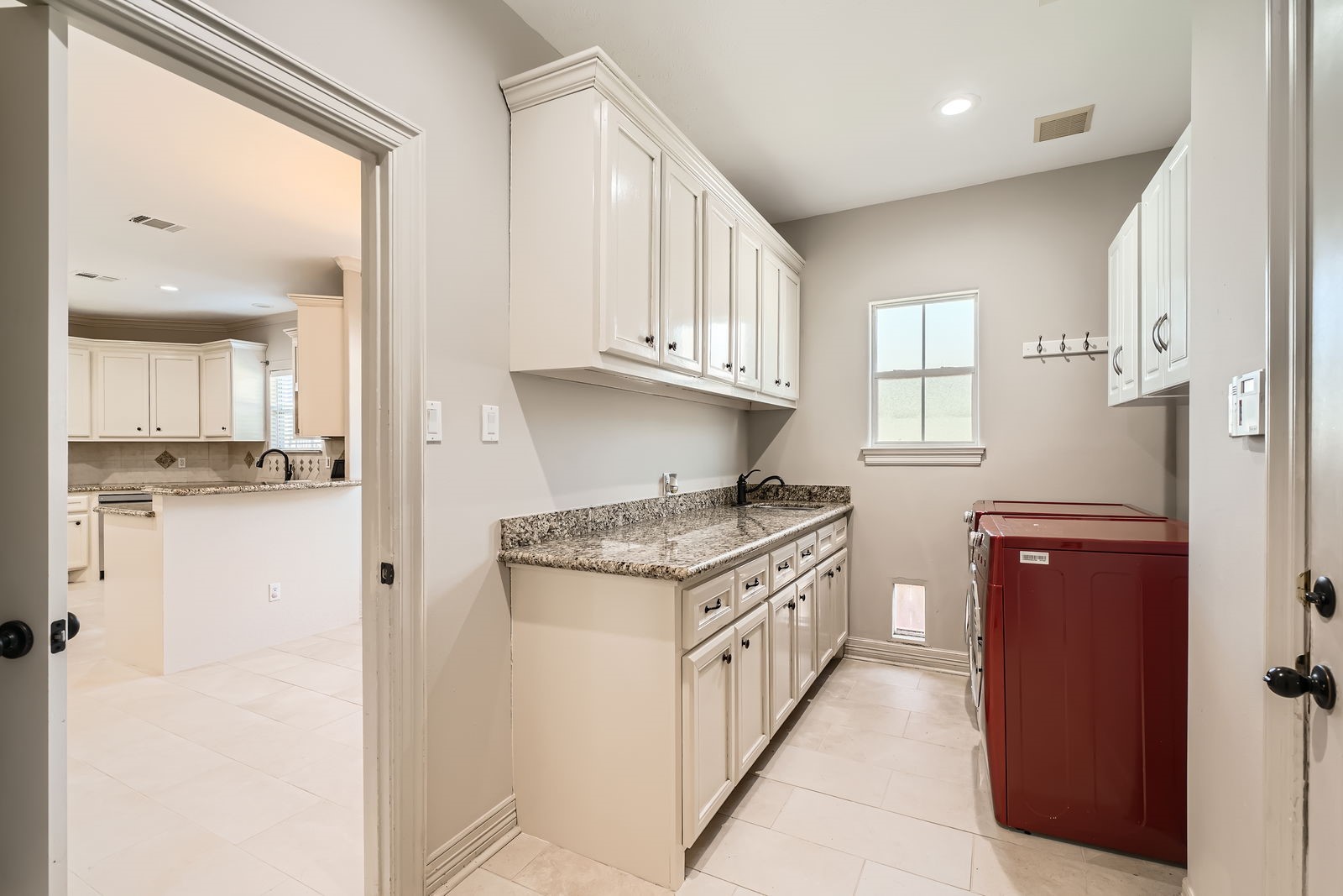 806 East 29th Street Houston, TX 77009 - Photo 23 of 30 This photo showcases a bright and spacious laundry room with ample counter space, granite countertops, and upper cabinetry for storage. A washer and dryer are neatly positioned along one wall. The adjacent kitchen area is visible, featuring matching cabinetry and a seamless flow between spaces.