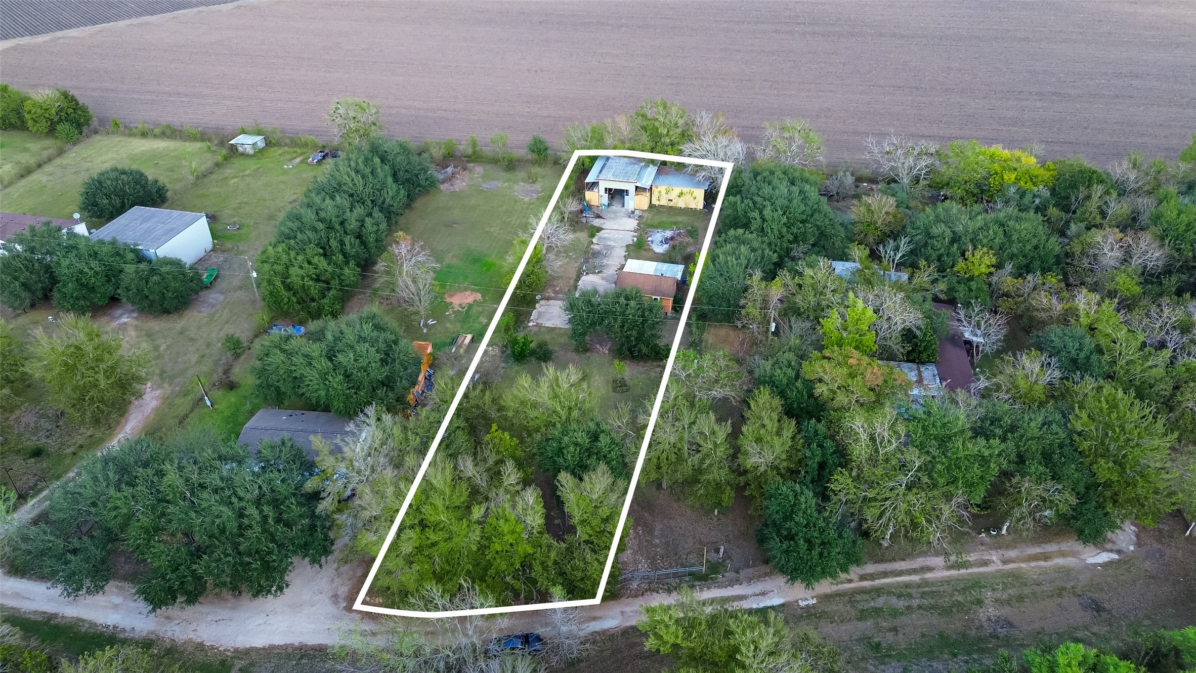 This aerial view shows a spacious rectangular plot outlined in white, surrounded by lush greenery and trees. The property includes a house and some outbuildings, offering privacy and a rural setting. Ideal for those seeking a serene, nature-filled environment.