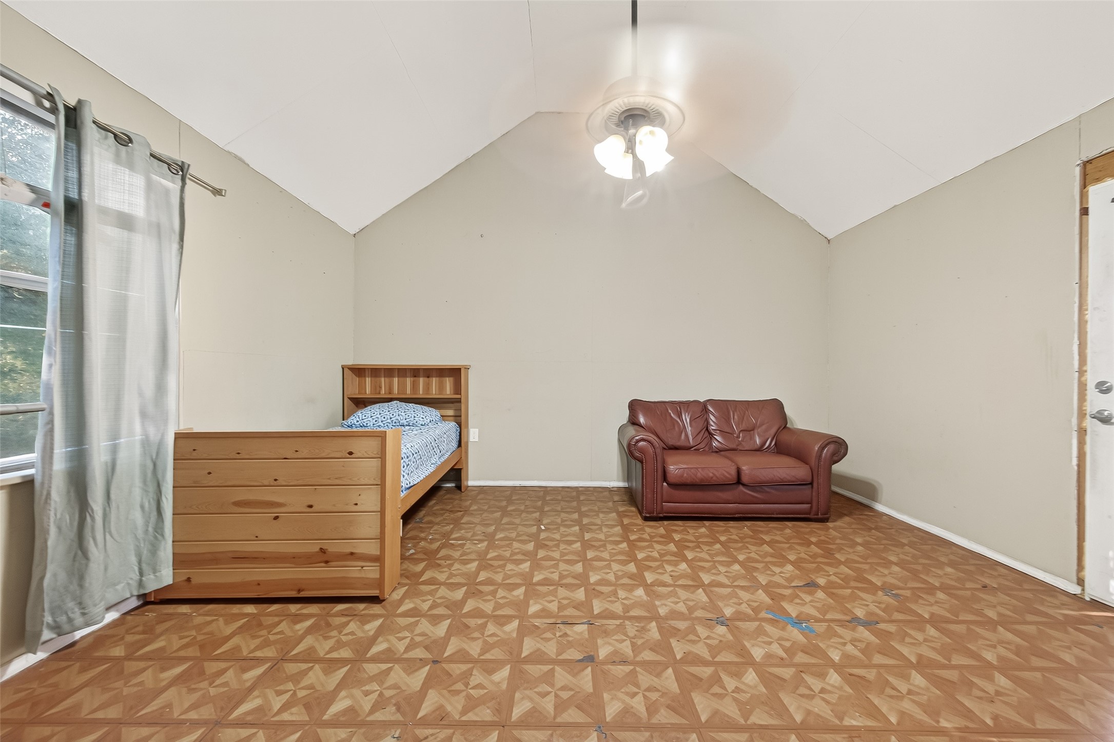 0 Quail Trail Beasley, TX 77417 - Photo 12 of 25 This spacious room features a high ceiling with a ceiling fan, patterned flooring, and a window for natural light. It includes a single bed and a leather loveseat, offering versatile use as a bedroom or additional living space.