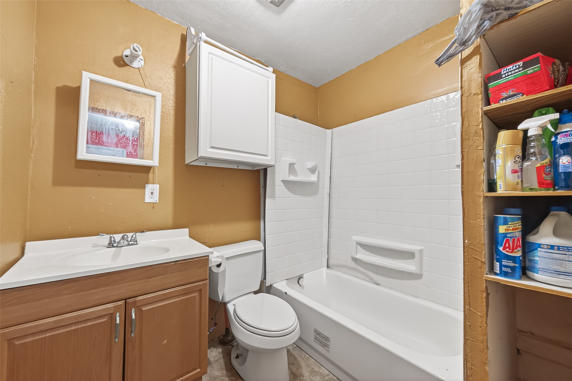0 Quail Trail Beasley, TX 77417 - Photo 16 of 25 This bathroom features a compact design with a bathtub and shower combination, a vanity with storage, and an overhead cabinet for additional space. It has a warm color scheme and built-in shelving for convenience.