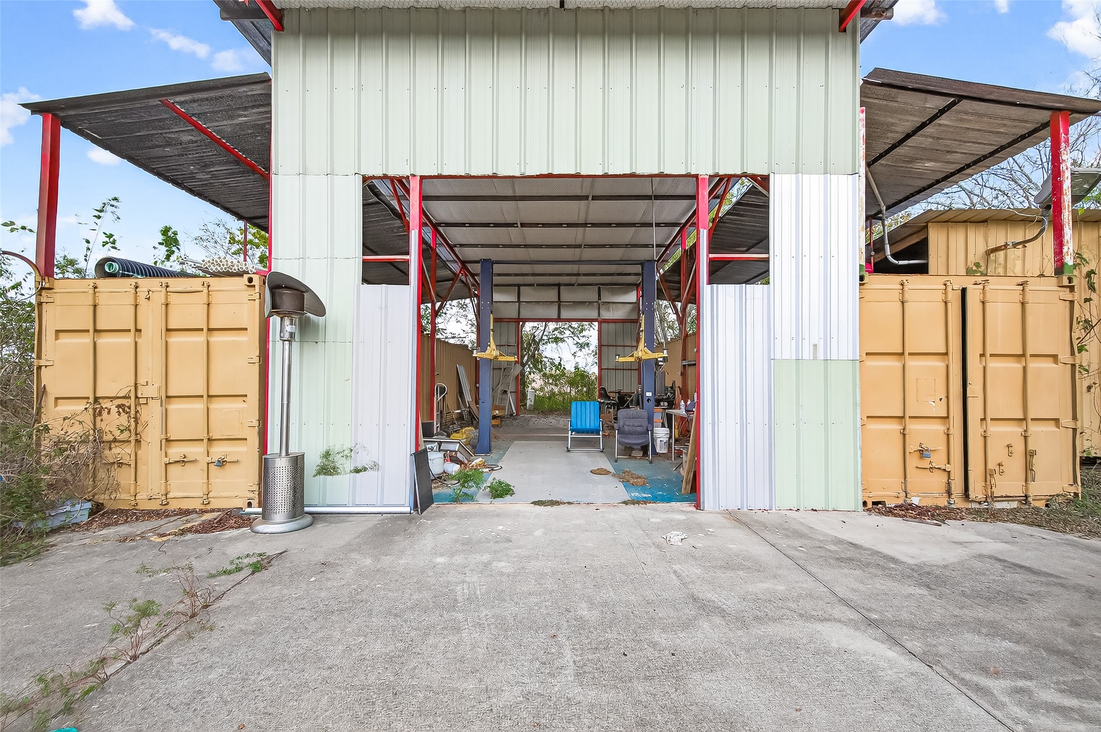 0 Quail Trail Beasley, TX 77417 - Photo 17 of 25 This photo shows an open, industrial-style structure with corrugated metal and shipping containers, featuring a spacious interior suitable for storage or a workshop. The area is paved, with a partially covered roof and ample natural light.