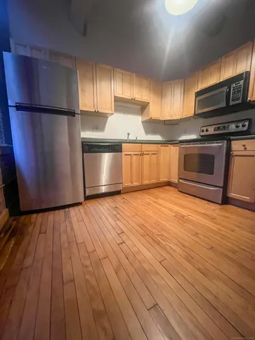 a kitchen with granite countertop wooden floors stainless steel appliances and sink