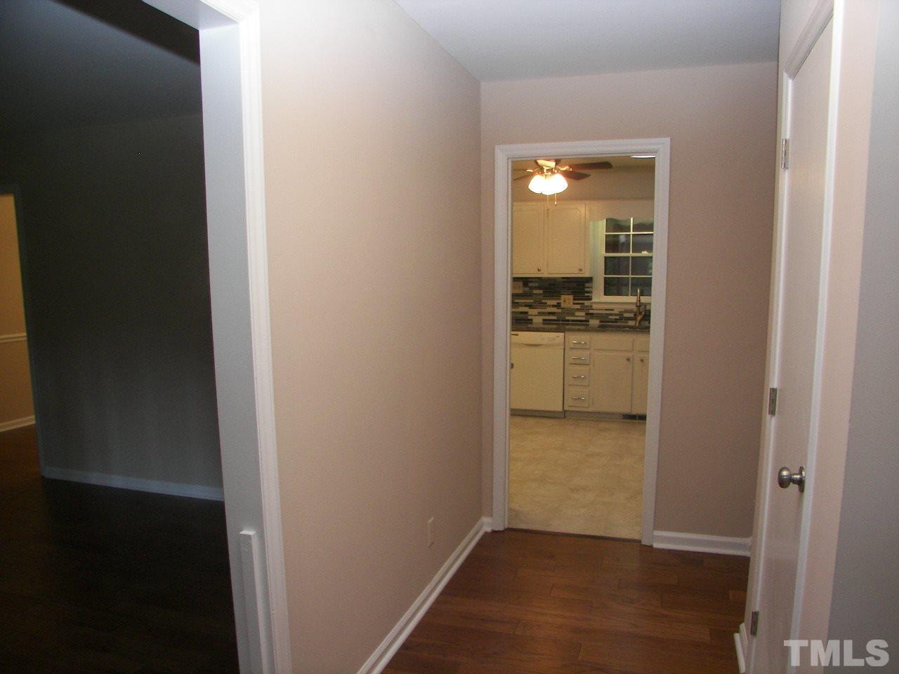 6729 Johnsdale Road Raleigh, NC 27615 - Photo 3 of 25 a view of a hallway with wooden floor and a kitchen space with a sink