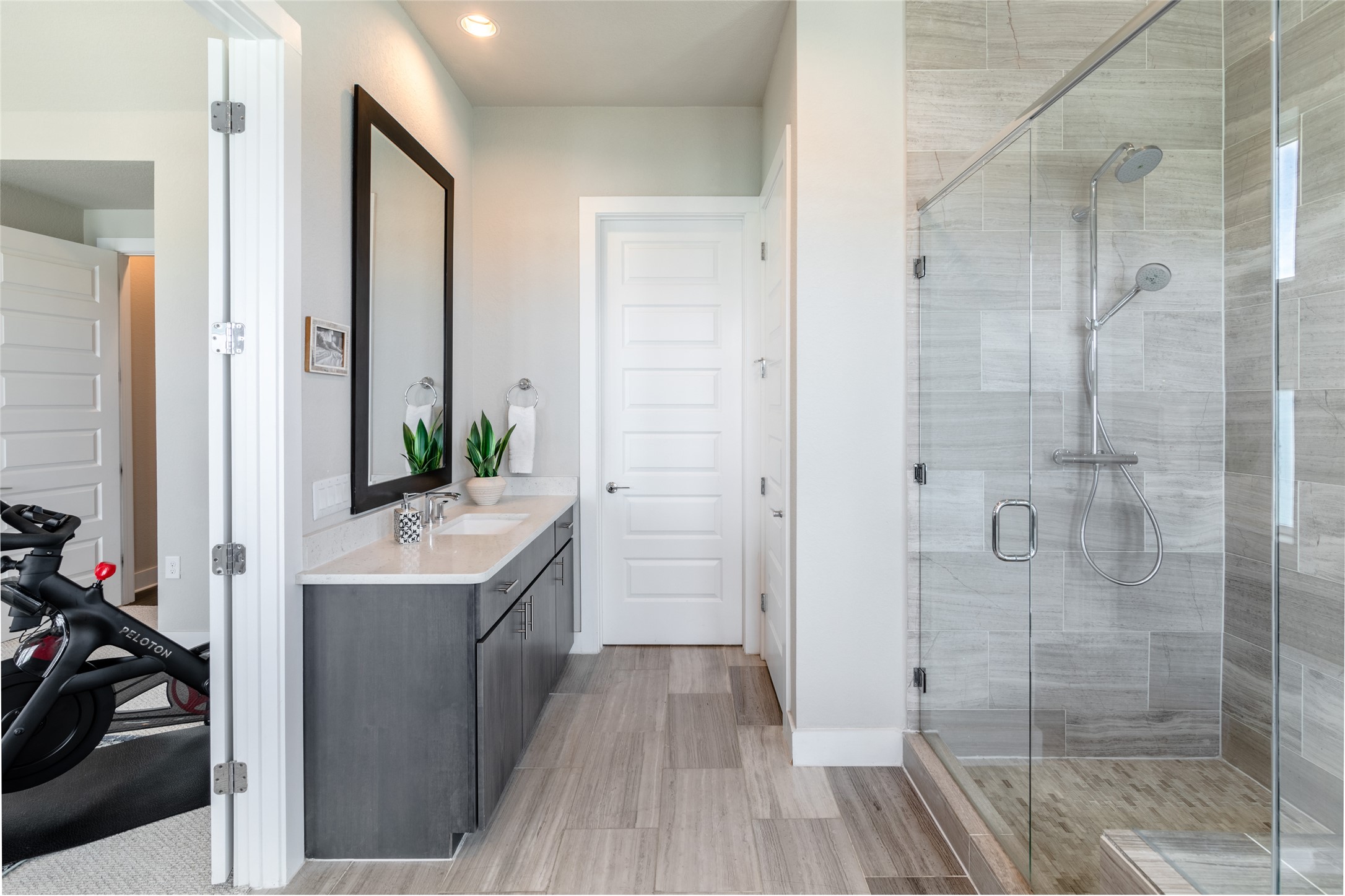 6025 Seville Drive Austin, TX 78724 - Photo 18 of 40 Spacious bathroom featuring a dual vanity with undermount sinks, a large framed mirror, wood-finish flooring, and a glass-enclosed shower with tile surround and dual shower heads
