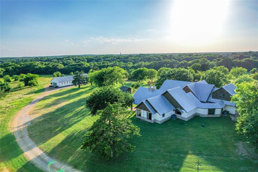 1922 A Bethel-Cannon Road Whitewright, TX 75491 - Photo 22 of 40 Expansive property featuring a multi-level residence with a metal roof and stone accents, surrounded by mature trees and manicured lawns